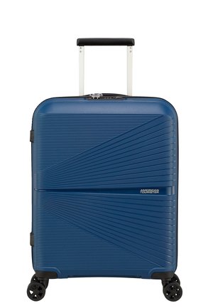 Valigia rigida blu con superficie testurizzata, manico telescopico, quattro ruote e etichetta con logo frontale. Design compatto e rettangolare.