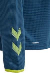 Maglietta sportiva a maniche corte con motivo blu, caratterizzata da disegni a forma di chevron riflettenti in verde e un bordo giallo sull'orlo, etichettata "BEECOOL."