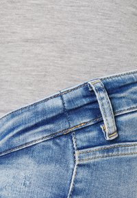 Sinine teksapükste vöökoht ja vööaasa lähedalt, taustaks helehall kangas.