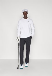 Bílé dlouhé rukávy, tmavě šedé kalhoty, bílé golfové boty s modrými akcenty a bílá čepice. Golfová hůl v pravé ruce, bílá rukavice na levé.