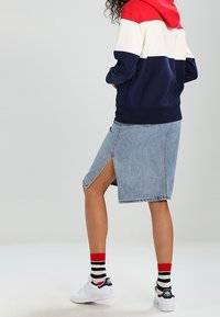 Sweat à capuche avec un bloc de couleurs rouge, blanc et bleu marine, associé à une jupe en jean clair avec une fente latérale. Porté avec des chaussettes rayées et des baskets.