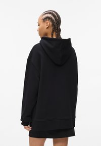 Black oversized hoodie with a back pocket and adjustable drawstring hood, made of soft fabric. Features long sleeves and ribbed cuffs.