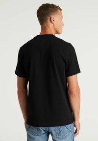 Crna pamučna majica kratkih rukava, s okruglim izrezom i ravnim krojem. Glatka tekstura, vidljivi šavovi i bez logotipa.