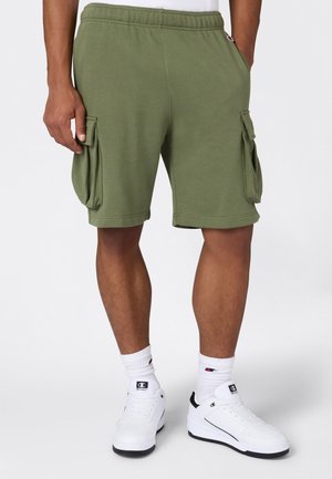 Olijfgroene cargoshorts met een elastische tailleband, zijzakken en een losse pasvorm, gecombineerd met witte sneakers en sportsokken.