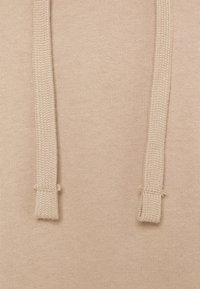 Tissu en coton beige à texture lisse, doté de deux cordons tirants sur le dessus, chacun présentant un design torsadé avec des extrémités finies.