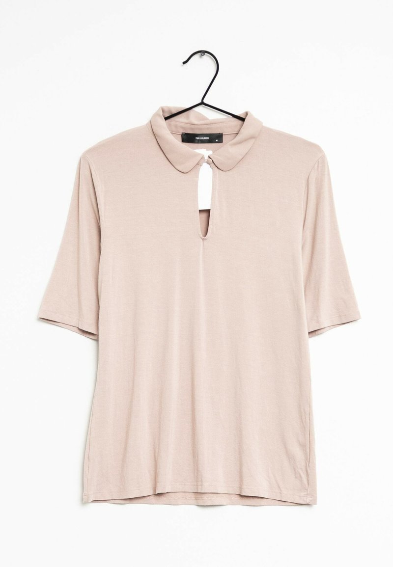 Blouse rose clair à manches courtes avec un col et une ouverture en forme de clé au niveau du cou. Tissu lisse avec une coupe décontractée. Suspendue à un crochet noir.