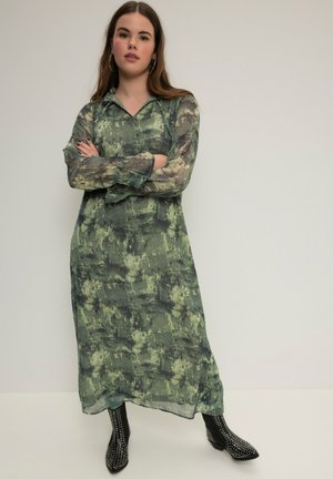 Lange, losse jurk in een groen en zwart abstract patroon, gemaakt van lichte stof met een V-hals en lange mouwen.
