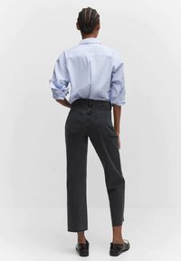 Camisa de manga larga azul claro, puños remangados. Vaqueros de pierna recta gris oscuro con cintura elástica. Zapatos planos negros. Diseño minimalista.