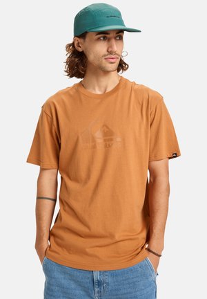 Brown cotton t-shirt with short sleeves featuring a subtle logo print on the front, paired with a green baseball cap. Soft texture, casual fit.