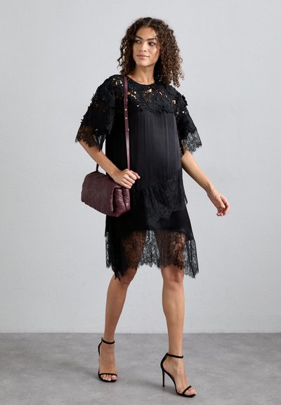Black dress featuring floral lace sleeves and hem, smooth fabric, asymmetrical design, paired with a burgundy crossbody bag.
