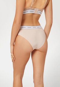 Beige Baumwollunterwäsche mit einem schwarz-weißen Markenelastikbund, der eine glatte Textur und einen mittelhohen Schnitt aufweist.