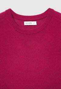 Magenta gestrickter Pullover mit rundem Rippstrickkragen und einem Etikett mit der Aufschrift "CALLIOPE S". Weiche Textur, mittleres Gewicht und gleichmäßige Farbe überall.