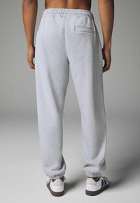 Hellgraue Sweatpants mit einem elastischen Bund, schmal zulaufenden Bündchen und einer einzelnen Gesäßtasche, kombiniert mit weißen und braunen Sneakers.