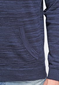 Navyblauer gestrickter Pullover mit strukturiertem Muster, Rundhalsausschnitt und seitlicher Tasche sowie Rippdetails am Saum und an den Bündchen.
