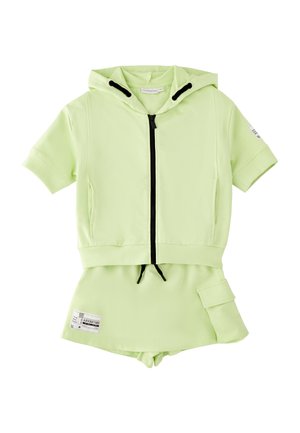 Jasnozielona krótka bluza z kapturem z czarnym zamkiem błyskawicznym i sznurkami, zestawiona z pasującą spódnicą z boczną kieszenią i nadrukowaną metką.