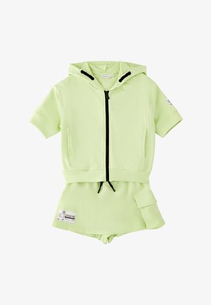 Sudadera con capucha verde claro de manga corta con cremallera negra y cordones, combinada con falda a juego con bolsillo lateral y etiqueta impresa.