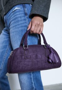 Lila Wildleder-Handtasche mit Krokodilprägung, doppelten oberen Tragegriffen, silbernem Zubehör und einem dekorativen Quastenanhänger mit Nieten.