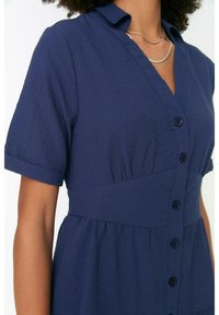 Mörkblå klänning i texturerad tyg, med knappslå framtill, korta ärmar, krage och en åtsittande midja.