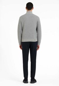 Maglione grigio lavorato a maglia con collo alto, abbinato a pantaloni blu navy e calzature nere, visto da dietro.