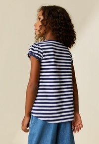 T-shirt rayé bleu marine et blanc avec manches courtes bouffantes et bordure en dentelle florale. Tissu en coton doux avec un ourlet arrondi.