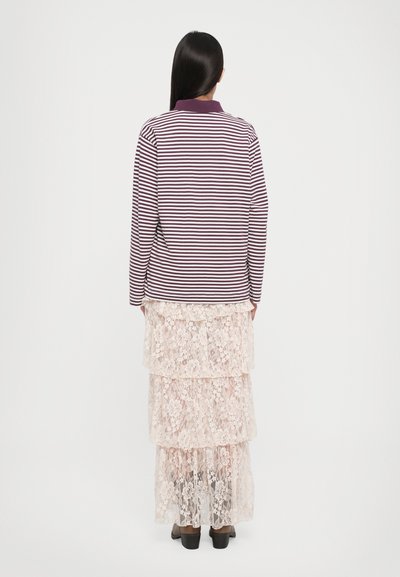 Langarm gestreiftes Poloshirt in Lila und Weiß, über einem mehrlagigen Spitzenrock in Hellrosa getragen, der florale Muster und einen fließenden Schnitt aufweist.
