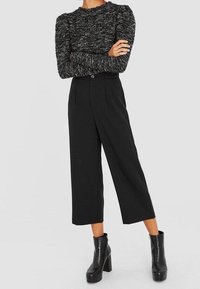 Suéter negro texturizado con mangas abullonadas combinado con pantalones negros de pierna ancha y alta cintura. El atuendo se completa con botas de tobillo negras de suela gruesa.