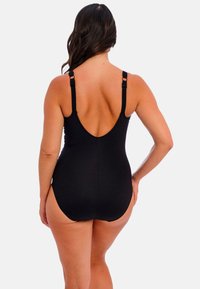 Mustan one-piece uimapuku, jossa on säädettävät olkaimet, matala selkädesign, sileä rakenne ja tiukasti istuva leikkaus. Ei näkyviä kuvioita tai korostuksia.