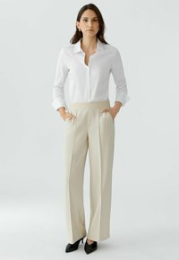 White button-up shirt, wide-leg cream trousers with a textured waistband. Black heeled shoes. Minimalist design, smooth fabric finish.