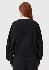 Sudadera negra de gran tamaño con mangas raglán, puños elásticos y dobladillo acanalado, que presenta una textura suave y un corte relajado.