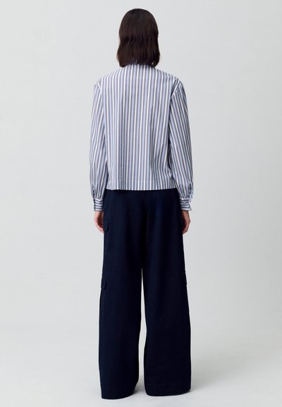 Camisa de manga larga a rayas en blanco y azul con una silueta cortada, combinada con pantalones anchos navy que tienen bolsillos tipo cargo.
