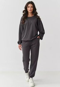 Ciemnoszara bluza i dopasowane dresy, wykonane z miękkiego materiału. Bluza ma wytłoczone logo, a dresy mają elastyczne mankiety.
