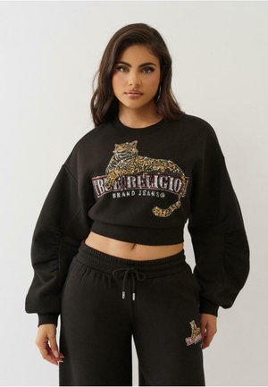 Schwarzes, kurzes Sweatshirt mit einem Leoparden-Print, verziert mit Strasssteinen, und mit Ballonärmeln, begleitet von einer passenden schwarzen Jogginghose.