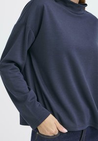 Mörk marinblå tröja med ståkrage, långa ärmar och en avslappnad passform. Slät tyg med minimal textur, inga synliga mönster eller detaljer.