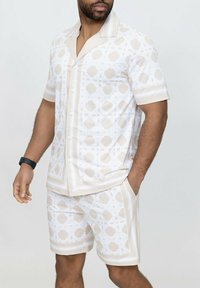 Ensemble chemise à manches courtes et short en beige et blanc avec des motifs géométriques et des accents rayés ; texture de tissu lisse.