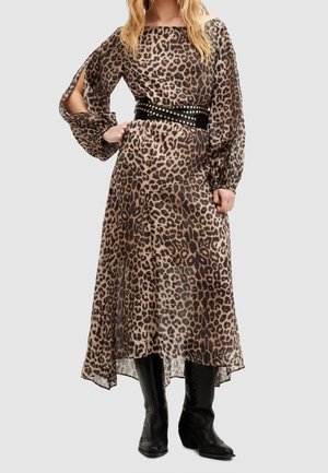 Woman wearing a long leopard-print dress with puffed sleeves and side slits, black studded belt, and black knee-high boots, standing.