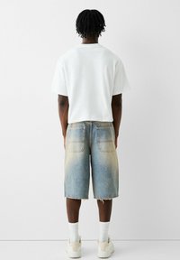 Camiseta blanca de manga corta con un corte relajado, combinada con shorts de mezclilla azul claro que presentan un degradado descolorido y dobladillo deshilachado.