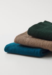 Drei gerollte Textilien in Dunkelgrün, Hellbraun und Blaugrün. Strukturiertes, gestricktes Material mit sichtbaren Nähten und einem weichen Erscheinungsbild.