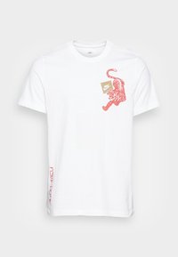 Vit bomull t-shirt med en röd tiger grafik och Nike-logotyp. Visar text i rött längs den nedre sidan. Korta ärmar, rundad halsdesign.