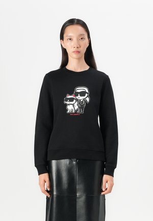 Sudadera negra con un estampado de dibujos animados de un gato y una persona con gafas de sol, con acentos rojos y puños y dobladillo acanalados.
