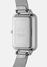 Montre en acier inoxydable avec un boîtier rectangulaire, un bracelet en maille et un dos gravé comprenant un numéro de série et le logo de la marque. Résistante à l'eau jusqu'à 3 ATM.