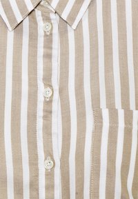 Beige och vit randig skjorta med knäppning, som har en krage, framficka och fyra vita knappar med en texturerad tygfinish.