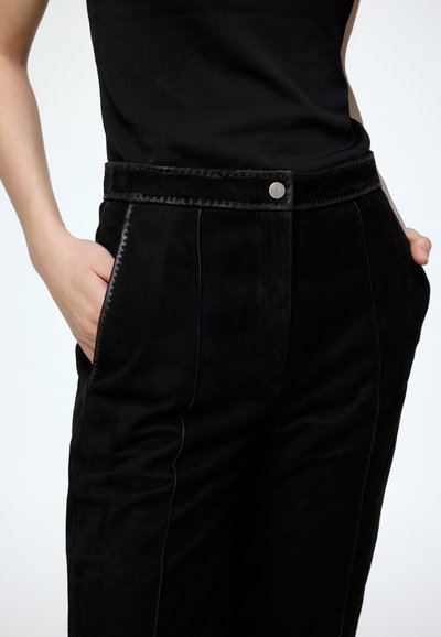 Zwarte suède broeken met een hoge taille, voorzien van een glanzende knoopsluiting, zijzakken en contrasterende stiksels langs de naden.