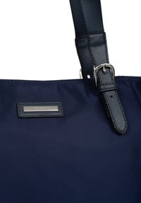 Marineblauwe totebag met een glad nylon lichaam, een gestructureerde leren accent en een logo-detail van zilveren hardware. Verstelbare schouderband voor veelzijdig dragen.