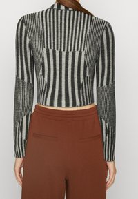 Pullover accorciato con righe verticali alternate in nero e grigio con una finitura testurizzata. Abbinato a pantaloni a vita alta color ruggine.