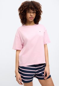 Rosa Baumwoll-T-Shirt mit lockerem Schnitt und kurzen Ärmeln, kombiniert mit marineblauen und pink gestreiften Shorts. Das T-Shirt ist mit einem kleinen Logo versehen.