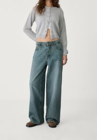 Light gray cropped cardigan with ribbed texture and button closure, paired with wide-leg light blue jeans and brown footwear.