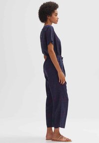 Marineblauwe jumpsuit met verticale strepen in rood en roze. Korte mouwen, elastische taille en drukknoopsluiting op de achterkant. Platte sandalen.