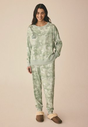 Ljusgrönt avslappnat set bestående av en sweatshirt med rund hals och tapered byxor med vita mönster av månar, stjärnor och geometriska former; mjuk textur.