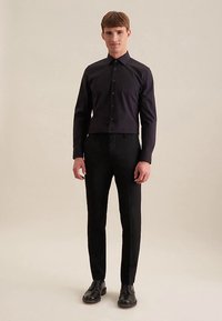 Zwarte blouse met knopen en een kraag, gecombineerd met op maat gemaakte zwarte broek en zwarte schoenen. Gladde stof met een strakke pasvorm.