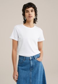 Balta medvilninė marškinėliai su trumpomis rankovėmis, apvaliu kaklu, derinami su mėlynomis džinsinėmis sijonais, turinčiomis aukštą liemenį ir priekine siūle.